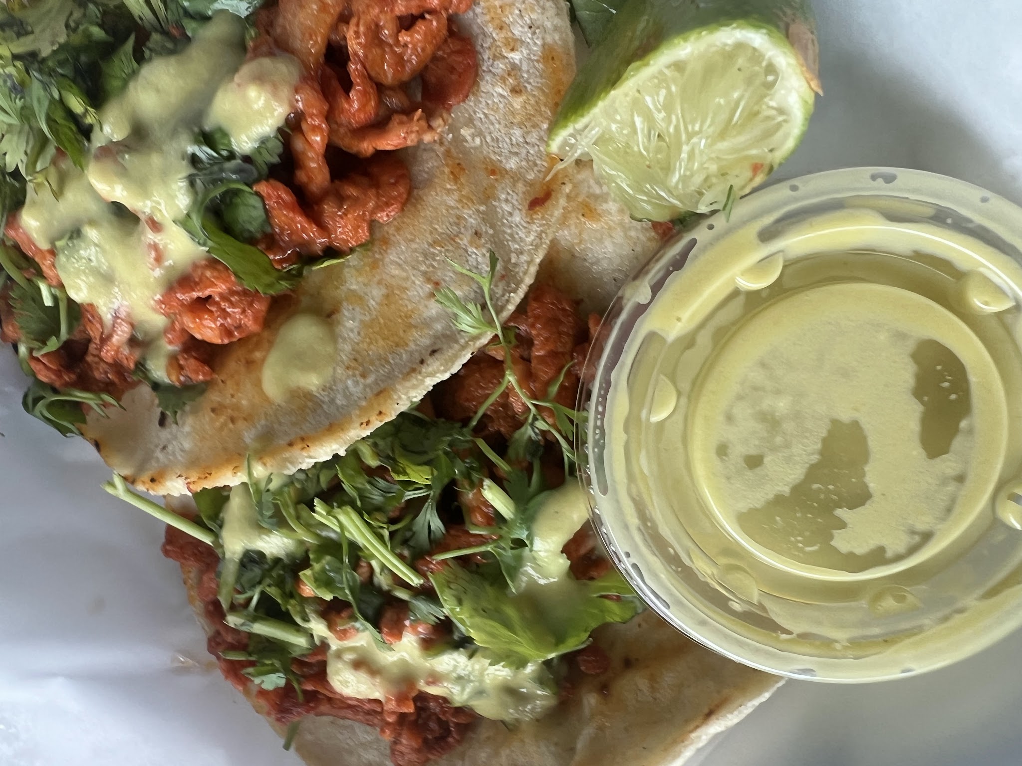 Two tacos al pastor topped with cilantro and green sauce, with a lime wedge