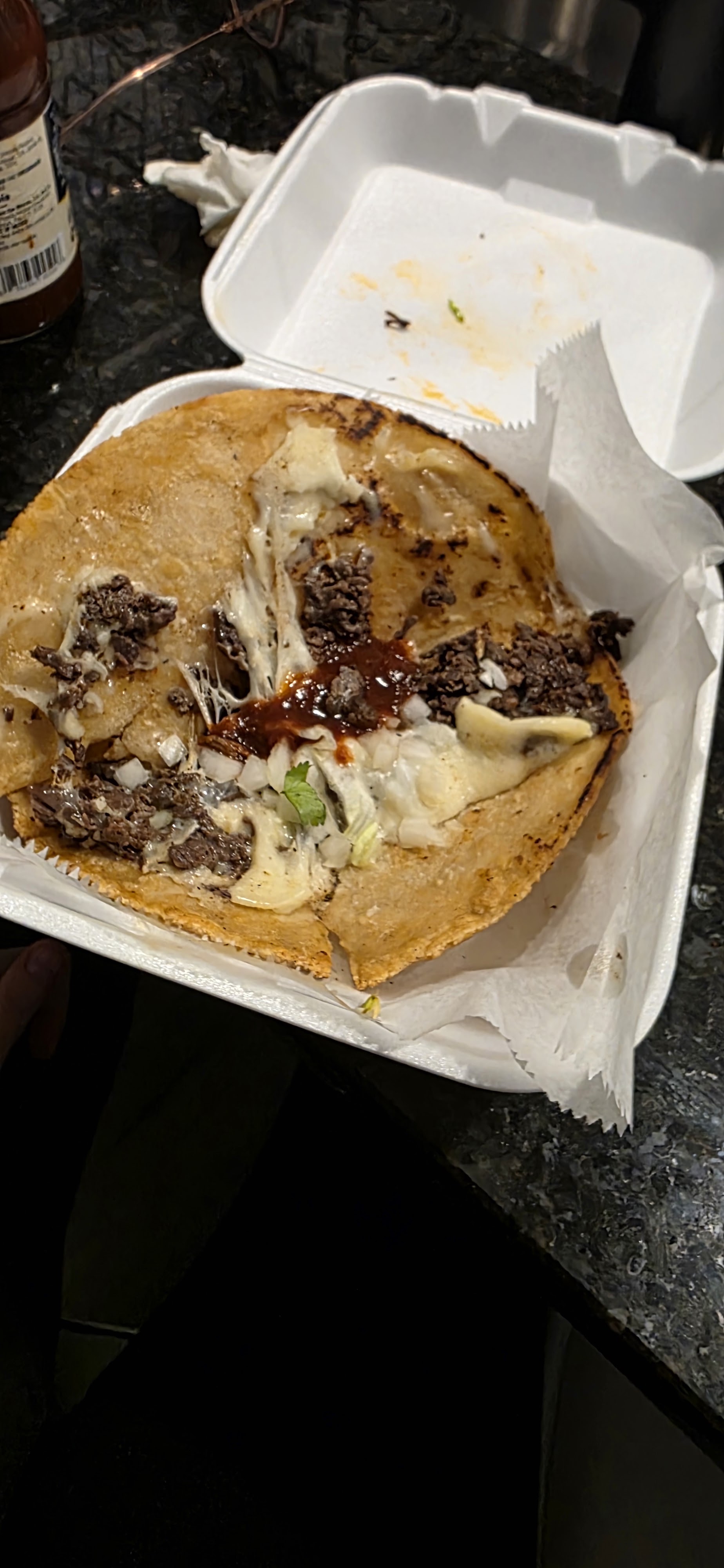 A birria taco with melted cheese in a takeout tray